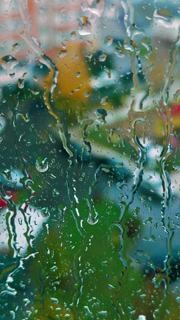 Raindrops hitting the window. View of the yard through the blurred glass in high-rise building. Vertical video