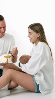 Happy Caucasian couple celebrating the first month anniversary being parents. Woman is holding a newborn in hands. Man lighting a candle on the cake. Vertical video
