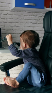 Tiny kid sitting in a big leather chair. Baby turns the chair to put remote control on the table. Vertical video
