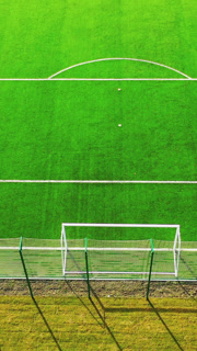 Green football pitch outdoors. Sport stadium for playing team game. Soccer field with artificial grass. Flying over the football field in sunny day. Vertical video