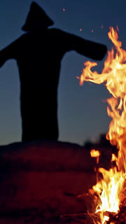 Scary figure in black mantle. Close up of witch stay around the fire in forest. Vertical video