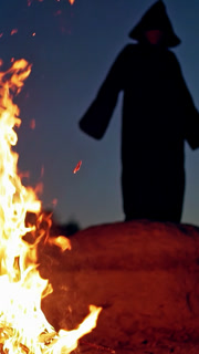 Terrible witch in the forest. Witch raising hand up near fire in forest. Vertical video