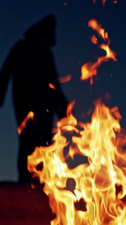 Witch on Halloween Day. Witch in cloak with hood near the fire in forest . Vertical video