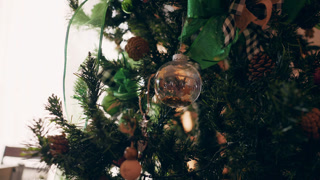 Warm cinematic close-up of a beautifully decorated christmas tree with pine cones, sparkling lights, ribbons, and a transparent bauble