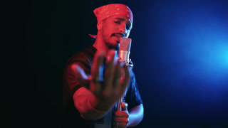 Young male artist singing and gesturing passionately into a professional studio microphone. Creative hispanic musician performing on stage