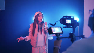 Talented woman singing into a condenser microphone while a cameraman records her performance. Backstage view of a professional music video