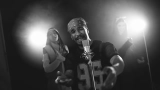 Male rapper singing and gesturing into a vintage microphone during a performance. Two backup dancers performing in the background with