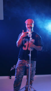 Talented rapper performing his song in a professional music studio. Cool male musician singing into a condenser microphone with blue