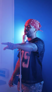 Young male artist with a red bandana rapping and gesturing energetically into a professional microphone in a blue lit music studio. Vertical