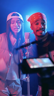 Young diverse couple of hip hop artists rapping and singing into a studio microphone while broadcasting a live video stream on social media
