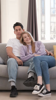 Young couple sitting on a sofa in their living room, posing happily for photos in a cozy and relaxed atmosphere