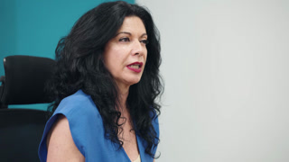 Experienced senior businesswoman with black hair talking and gesturing during a business meeting or interview in a modern office