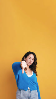 Unhappy young woman with curly hair expressing dissatisfaction. Her negative facial expression and thumbs down gesture show disapproval