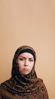 Upset young woman wearing a traditional hijab, looking at the camera with a sad and frowning expression. She is isolated on a beige