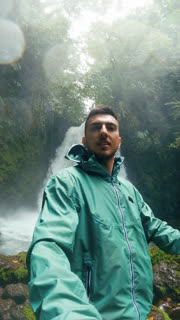 Young male content creator filming himself with a beautiful waterfall in the background at Arenal Volcano National Park, Costa Rica