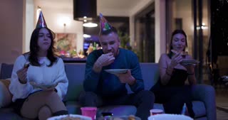 Friends Enjoying Pizza and Snacks at a Cozy Birthday Celebration with Party Hats and Festive Ambiance