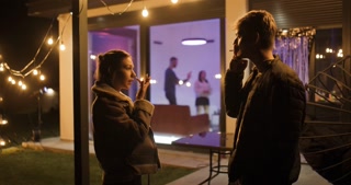 Friends Chatting and Smoking at a Lively Birthday Party with Fairy Lights and Dancing in the Background