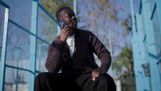 Young Man Talking on Phone by Basketball Court