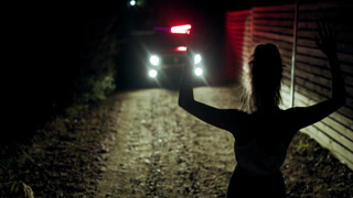 Girl with hands raised in front of police silhouette at night on a gravel road during an intense encounter