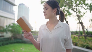 Asian woman reading stories in a serene setting with nature and modern architecture