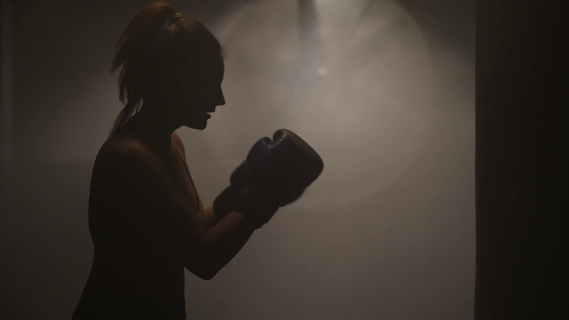 Silhouette woman fighter mma in boxing gloves hitting on punching bag