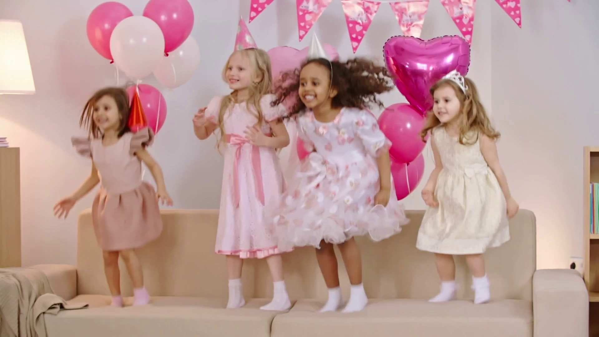 Four excited little girls with party hats on their heads jumping on
