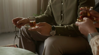 Close up shot of unrecognizable Muslim couple drinking tea together at home with focus on hands holding traditional tea glasses and praying beads, copy space