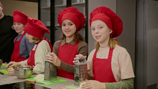 Slowmo portrait of Caucasian female teenagers wearing red chef hats and aprons, holding graters in kitchen. Footage is perfect for promoting culinary schools or children cooking classes