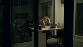 Wide shot of Hispanic female company worker walking into office to say goodbye to stressed Caucasian male colleague, working on deadline report late at night, patting on shoulder and departing home