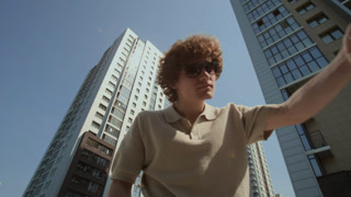 Pov of young adult Caucasian man with curly hair wearing sunglasses opening car trunk, putting on shoulder bag, and looking inside. Low angle shot perfect for automotive, travel, or lifestyle promo