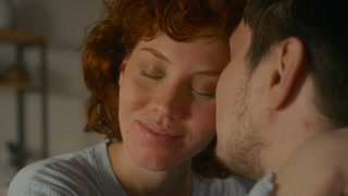 Candid close up shot of happy young couple kissing gently and cuddling in morning with focus on young woman enjoying affection