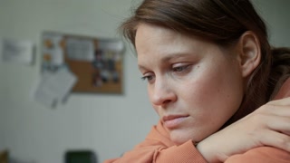 Closeup portrait of face of depressed, tearful young Caucasian refugee woman sitting in emergency accommodation, chin on knees, worrying about friends or family, after surviving disaster