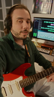 POV of Caucasian young male musician wearing headphones, holding electric guitar and talking to camera in home studio presenting new broadcast. For online music education or tutoring promos, vertical