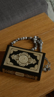 Vertical zoom in shot of Quran book decorated with intricate gold design lying on wooden table in traditional Muslim home no people