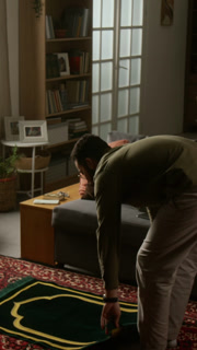 Vertical side view shot of adult Muslim man starting daily praying and laying mat down on floor in modern home setting with traditional decor elements