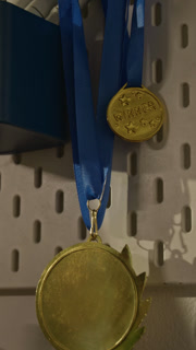 Vertical no people shot of gold winner medal with blue ribbon hanging on pegboard. Clip representing success, perfect for motivational corporate videos or sports achievement campaigns