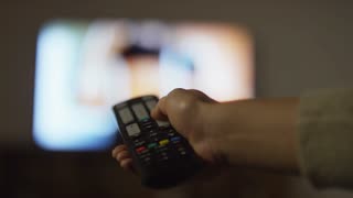 Close up shot of hands of unrecognizable woman holding remote control and changing channels on TV