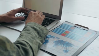 Close up shot of unrecognizable army officer typing on laptop. Document on clipboard lying on table
