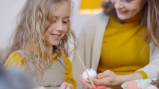 Handheld tracking of joyful parent showing hand-painted Easter egg to adorable child and conversing