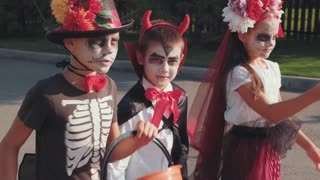 Handheld tracking shot of boys and girl in halloween costumes walking down street together while trick-or-treating in neighborhood