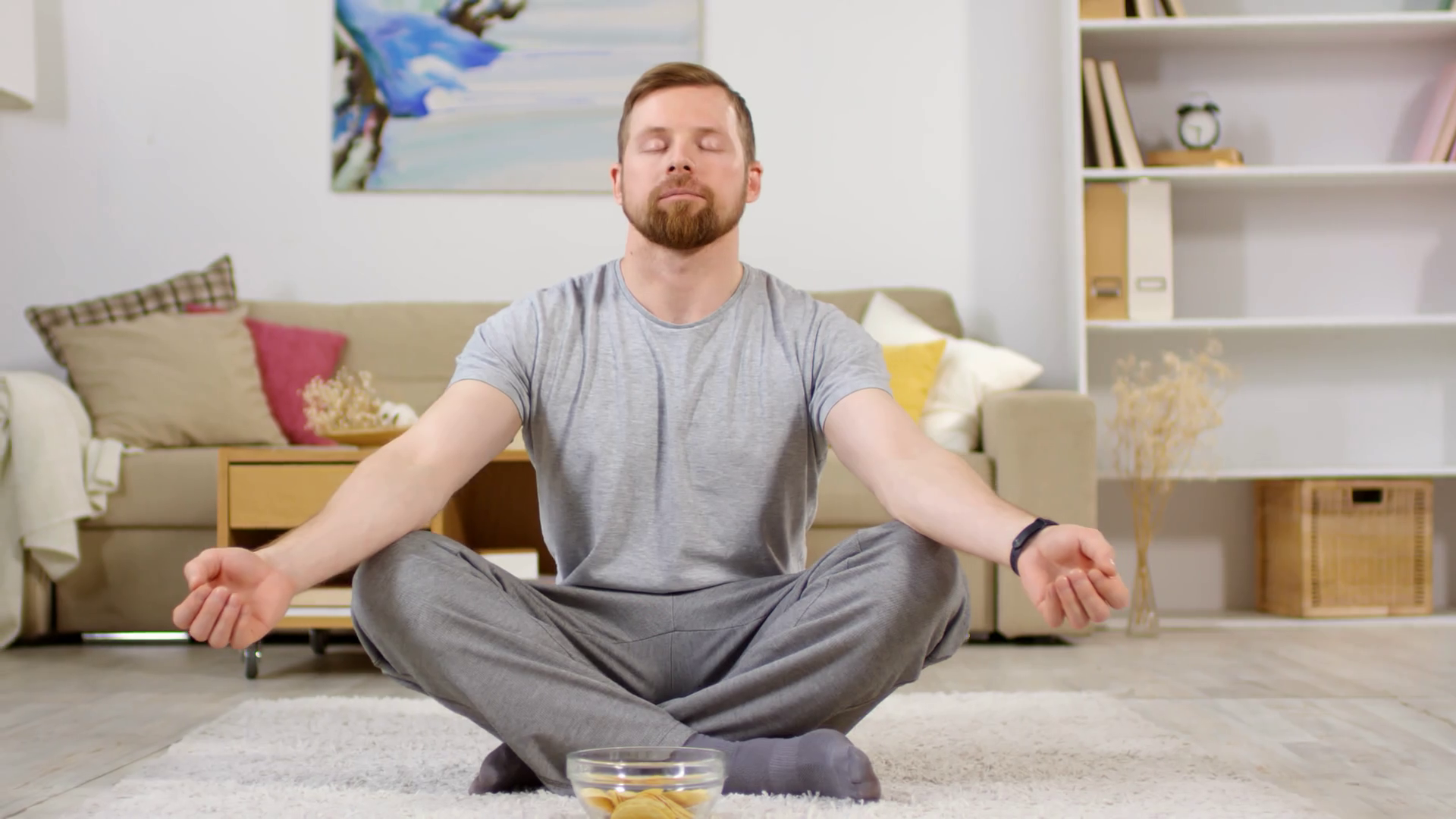 Man in sportswear sitting in lotus pose on carpet in the living room
