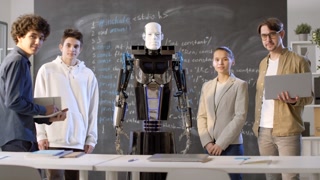 Medium portrait of information technology teacher with laptop, group of multi-ethnic classmates and quantum man-like robot in middle standing at blackboard looking at camera