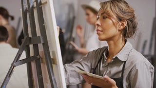 Medium shot of concentrated mixed-race woman creating abstract painting on canvas at group arts course in bright studio