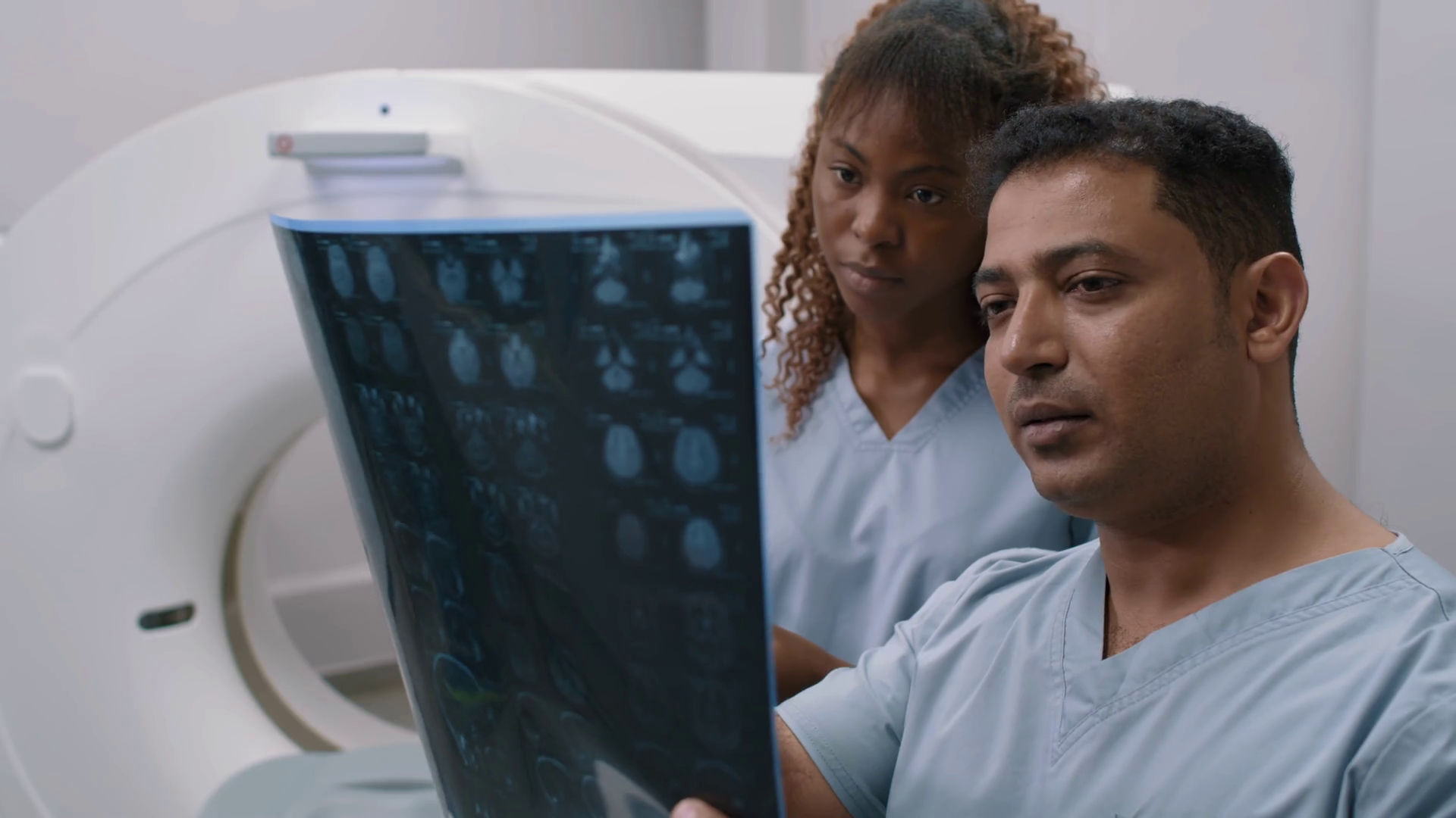 Medium shot of male radiologist in scrubs holding CT scan of brain and