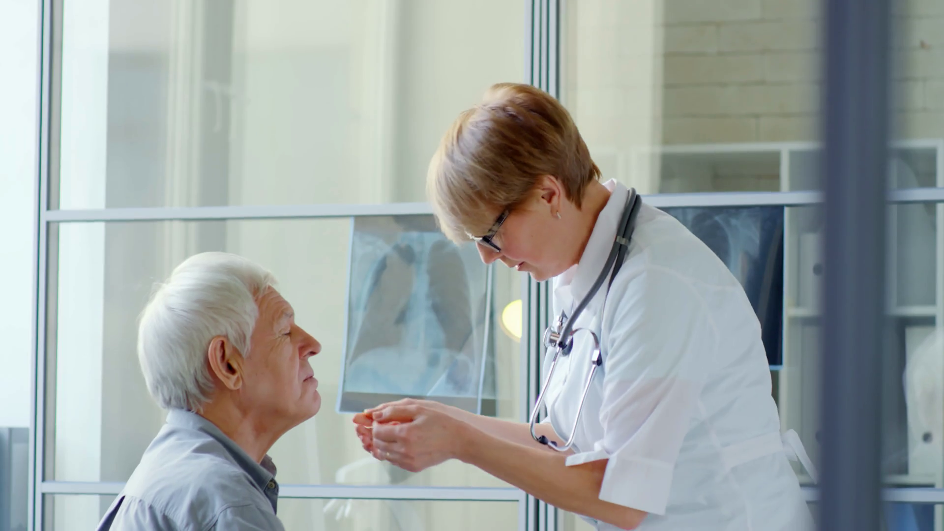 Middleaged female doctor checking throat of senior male patient with medical penlight during