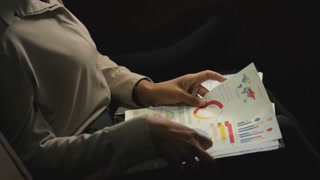 Midsection close-up of unrecognizable business lady looking through papers with charts and diagrams at backseat