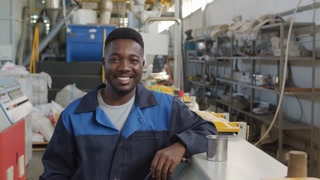 Portrait shot of cheerful African-American male factory worker smiling for camera in workplace