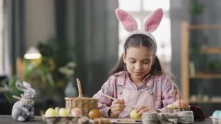 Portrait of girl in bunny ears painting Easter egg, smiling at camera