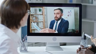 Tilt up shot of mid-aged businessman explaining documents and talking to colleagues from computer screen during online meeting