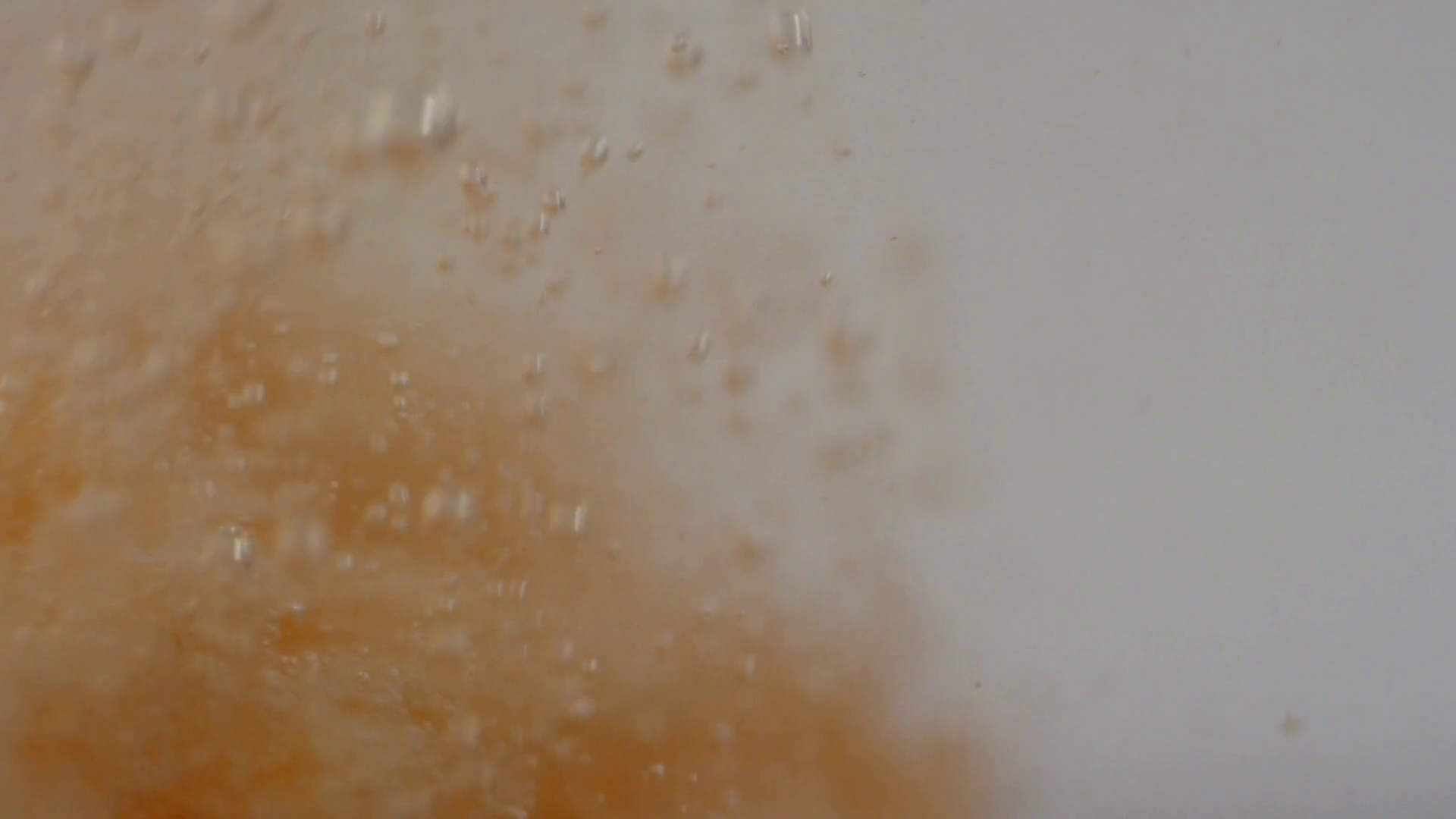 Underwater macro tracking shot of peachy bath bomb exploding and creating small bubbles in water
